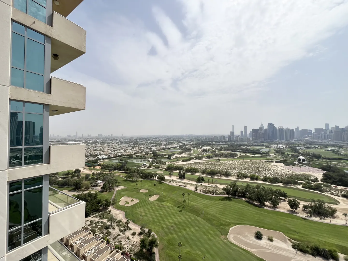View from a high-rise balcony overlooking a green golf course and a distant city skyline under a cloudy sky.