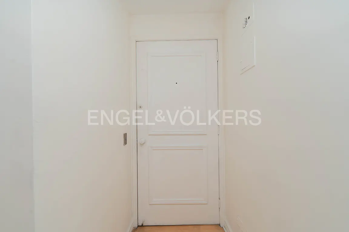 A white interior door with a peephole and simple paneling, centered between two plain white walls in a narrow hallway.