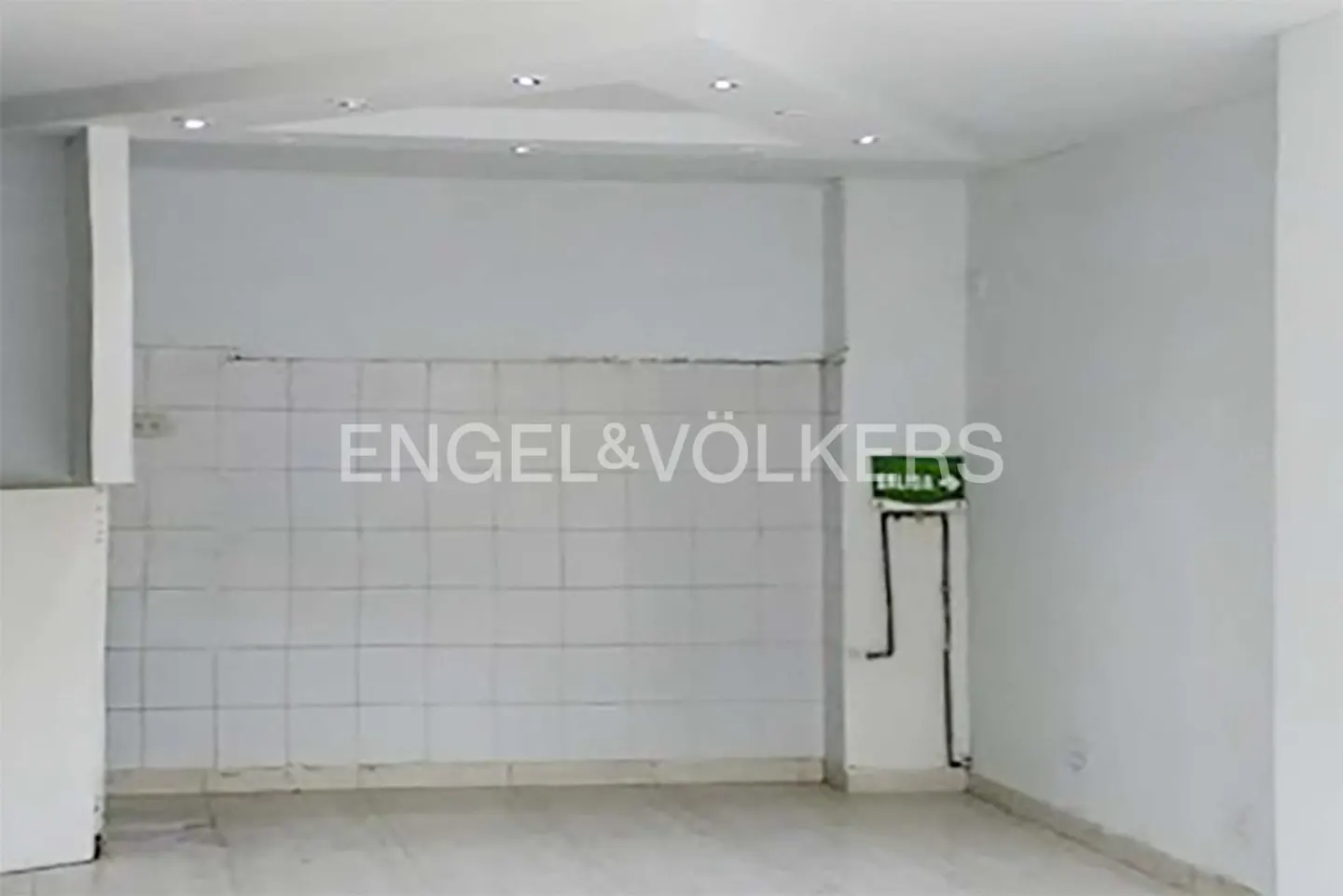 Empty white room with tiled wall, exit sign, and Engel & Völkers logo.