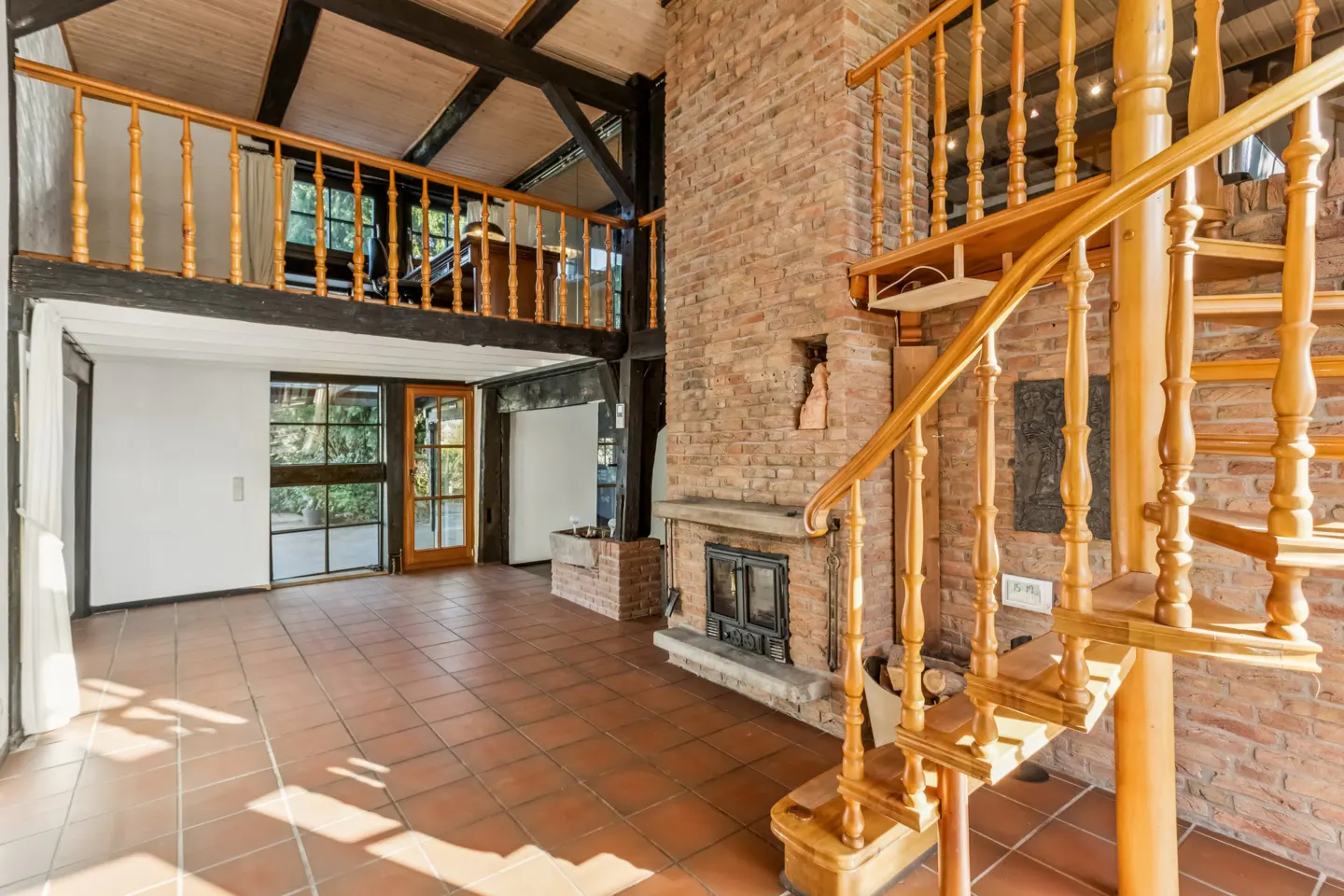 Interior view of a home featuring a brick fireplace, wooden spiral staircase, and a loft with a wooden railing.