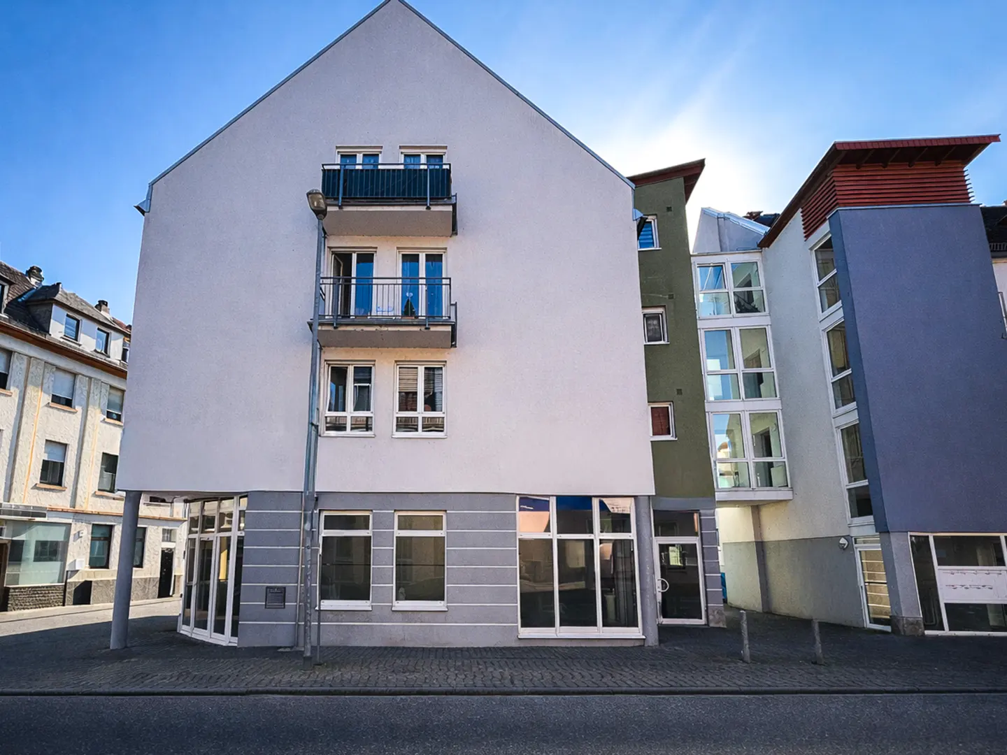 Modern apartment building with white facade, balconies, and large windows on a sunny day.
