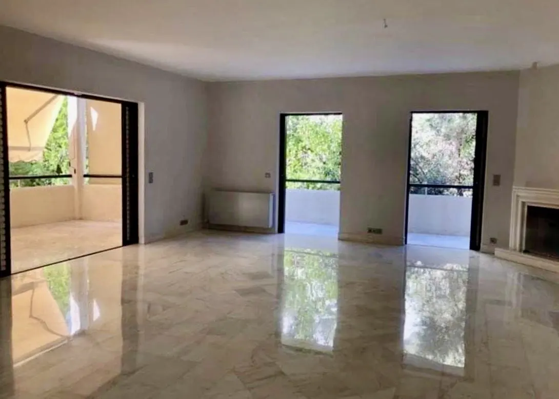 Bright, empty living room with marble floors, gray walls, and black-framed doors leading to balconies with green foliage views.