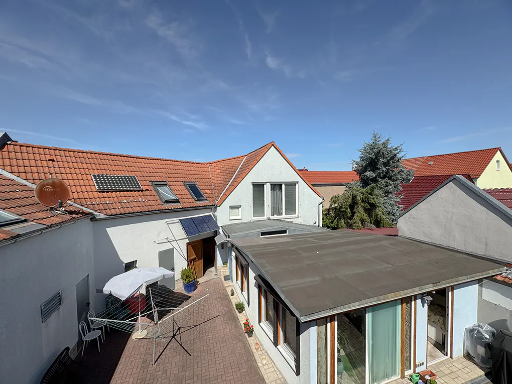 Aerial view of a courtyard with white buildings, red tile roofs, solar panels, and a clothesline under a blue sky.