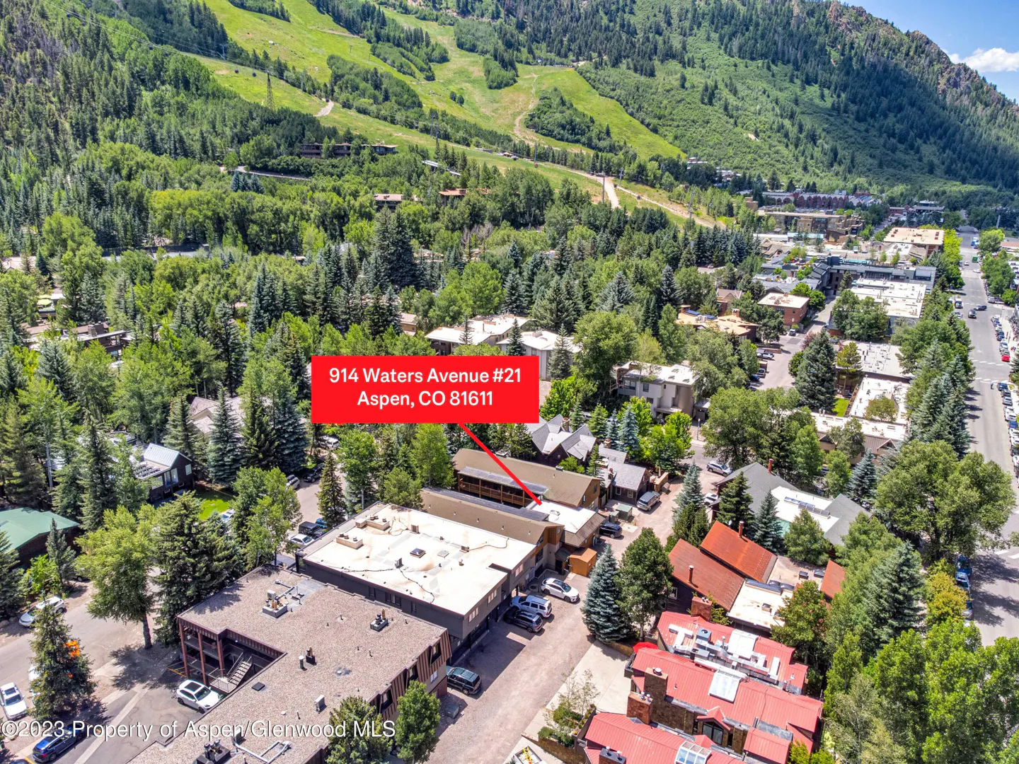 Aerial view of 914 Waters Avenue #21, Aspen, CO, surrounded by green trees and mountains. Buildings have flat and red roofs.
