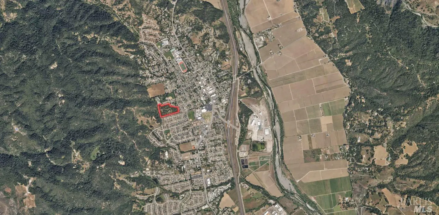 Aerial view of a town nestled between green hills and farmland, with a red outline highlighting a specific property.