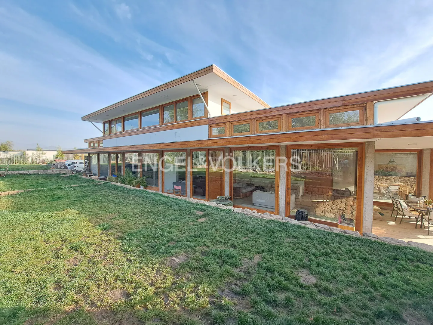 Modern two-story home with wood trim and large glass windows overlooking a grassy lawn under a bright blue sky.