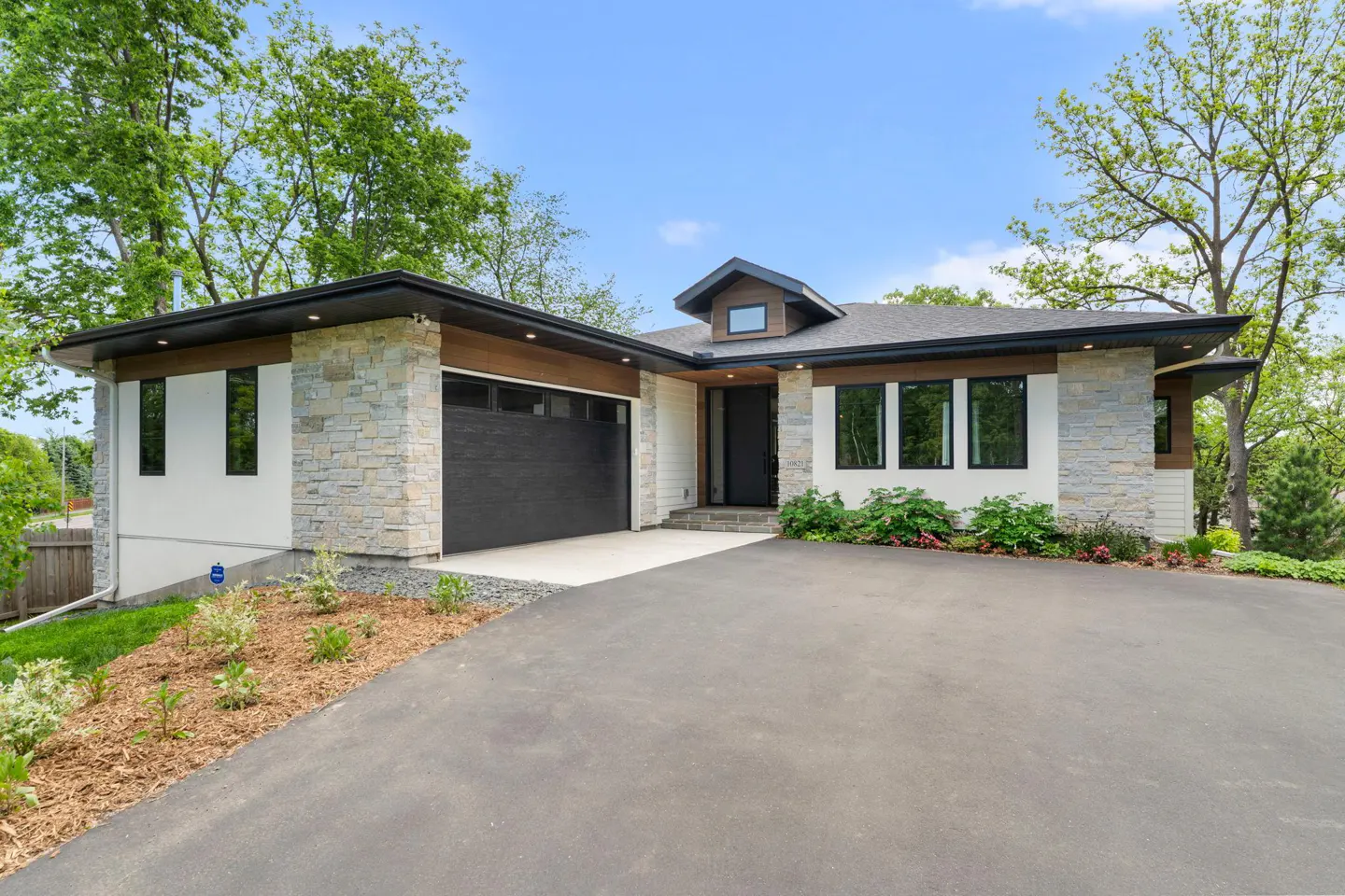Modern single-story home with stone and white siding, black garage door, and a paved driveway leading up to the house.