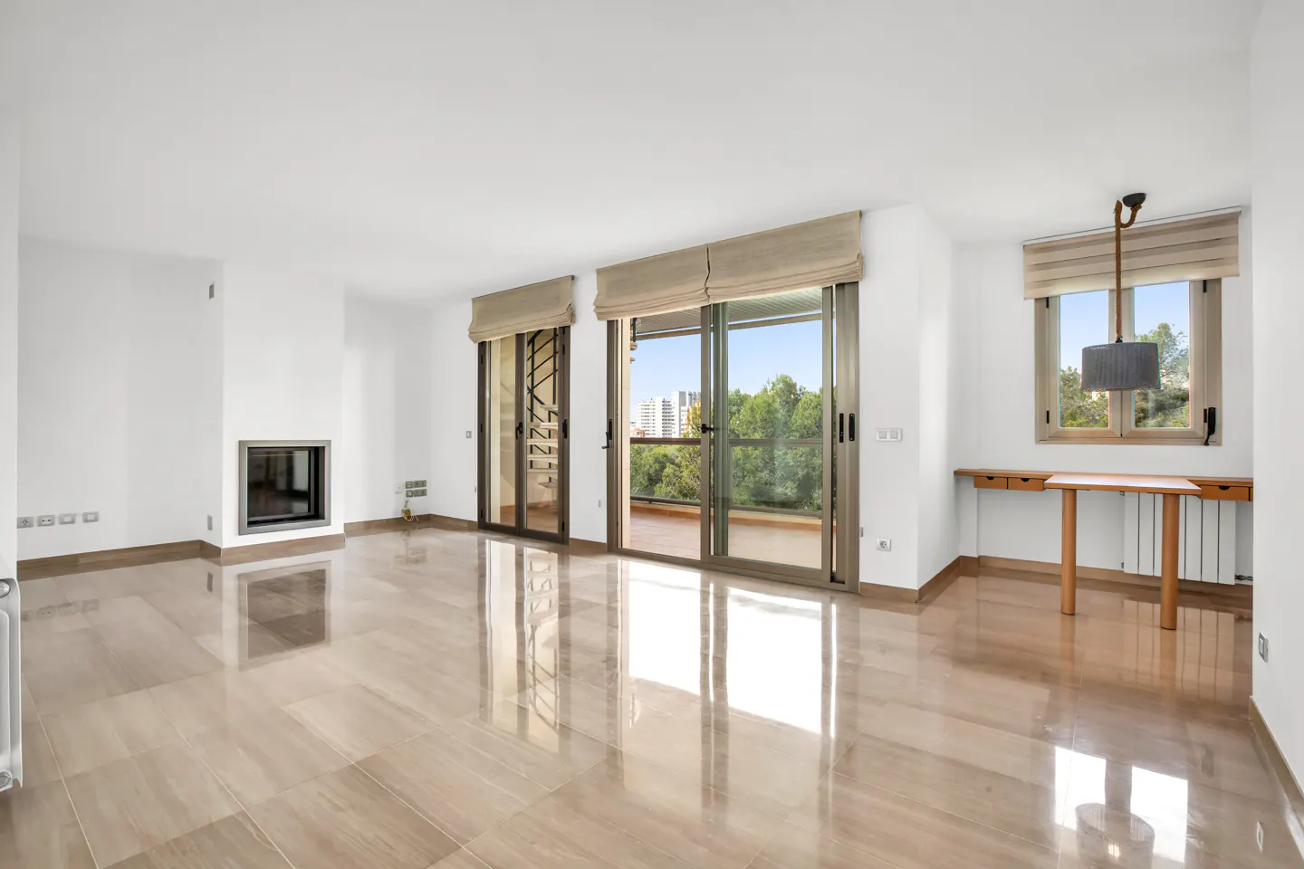 Bright, empty room with beige tile floors, white walls, fireplace, and sliding glass doors to a balcony with green trees.