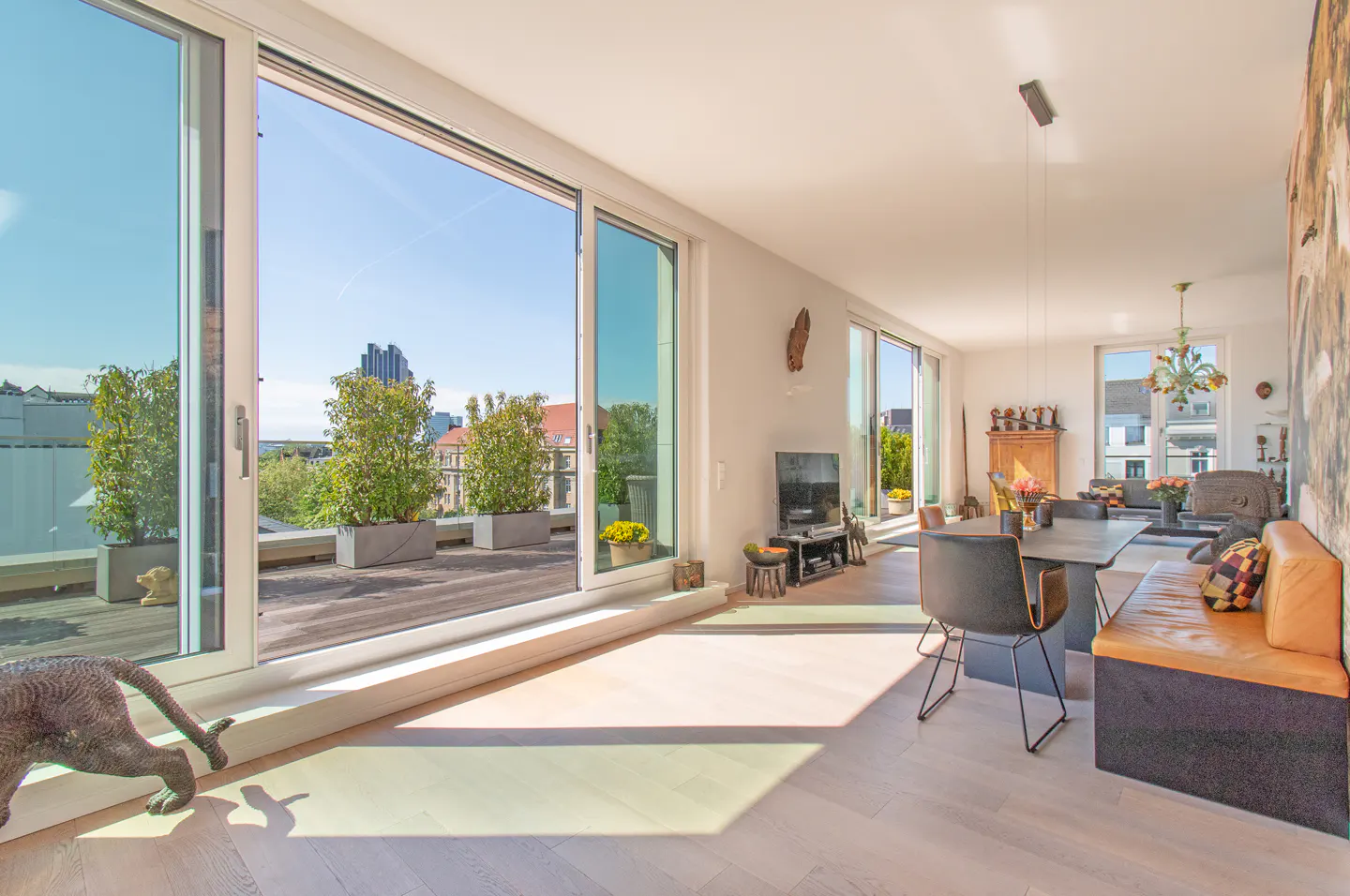 Bright, modern living room with a dining area, bench seating, and a large sliding glass door to a balcony with city views.