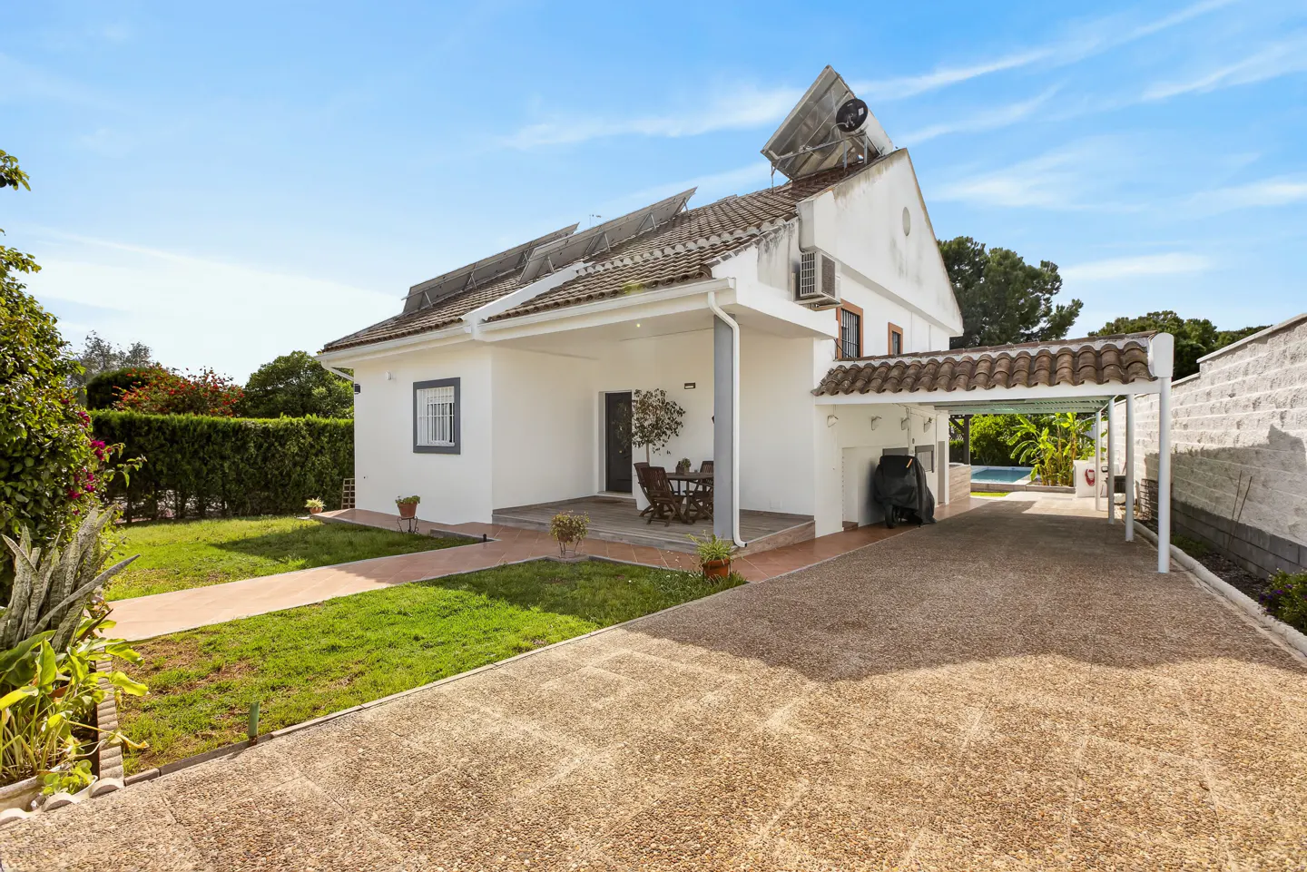 Exterior view of a two-story white house with solar panels, a covered patio, and a gravel driveway.