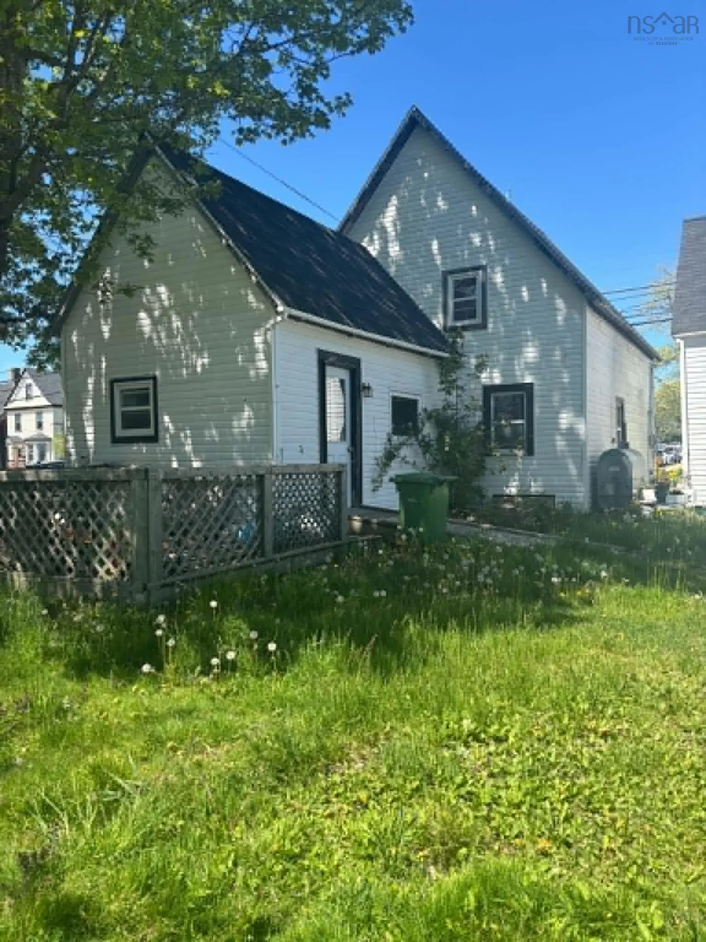 White two-story house with a dark roof, lattice fence, and grassy yard under a clear blue sky.