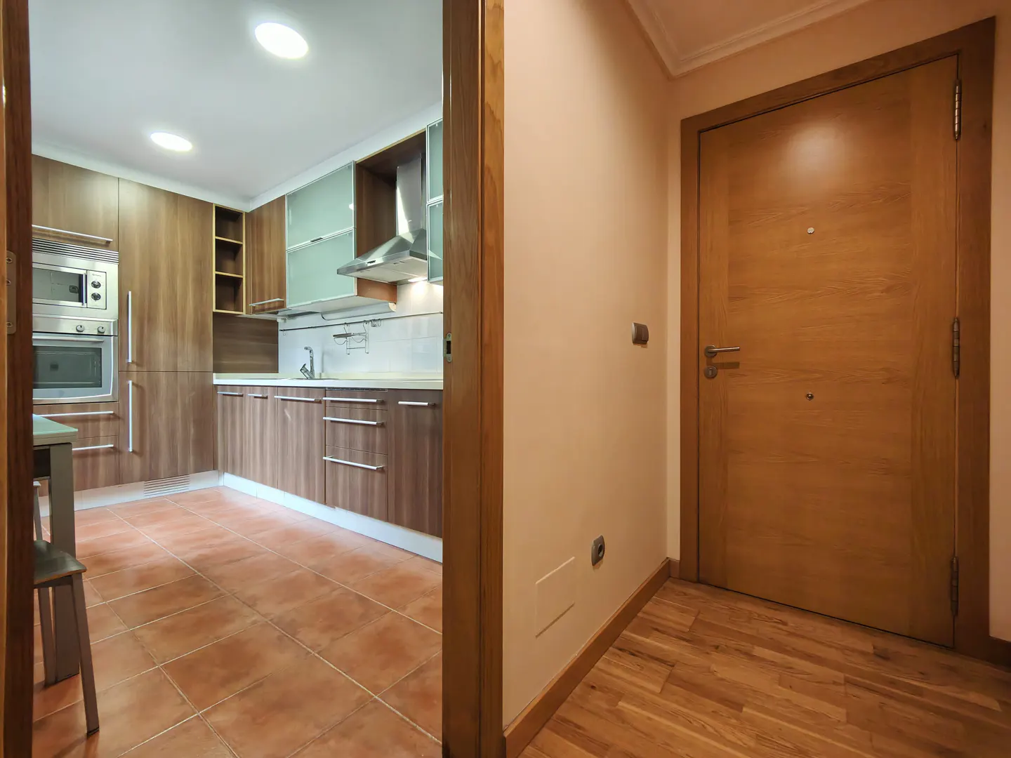 A view through a doorway into a kitchen with brown cabinets and tile floors, and a closed wooden door to the right.