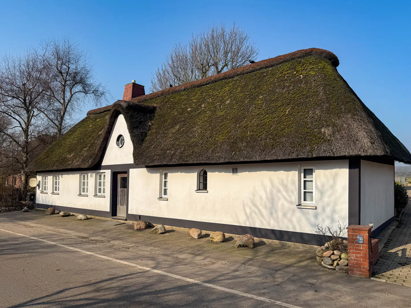 A white, one-story house with a thatched roof under a blue sky. The house has black trim and several windows.