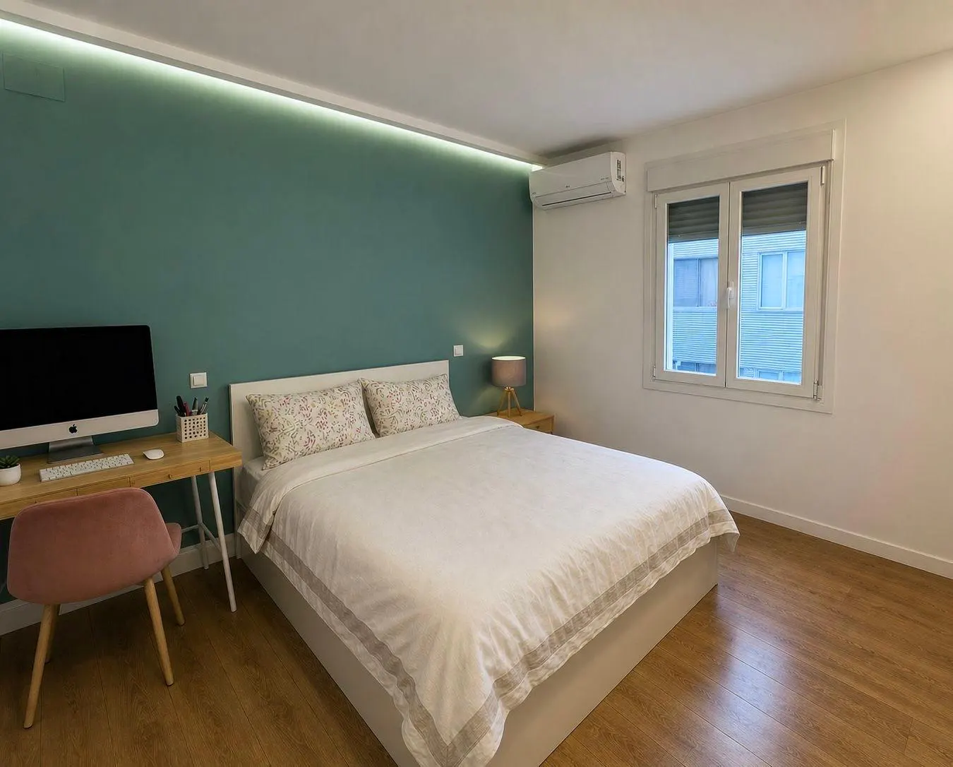 Bedroom with a double bed, desk with computer, pink chair, wood floor, and a teal accent wall.