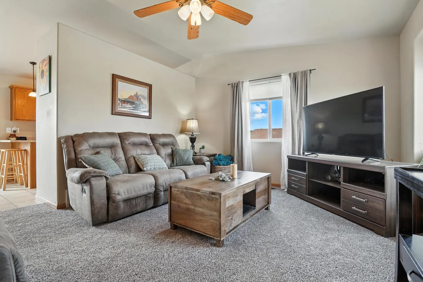 Living room with a brown reclining sofa, wooden coffee table, large TV on a media console, and a ceiling fan.