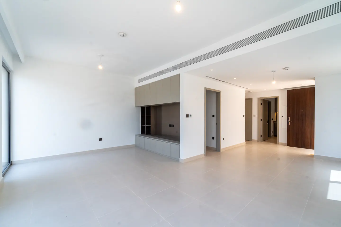 Bright, empty room with white walls, beige tile floor, and built-in gray shelving. Three doorways are visible.