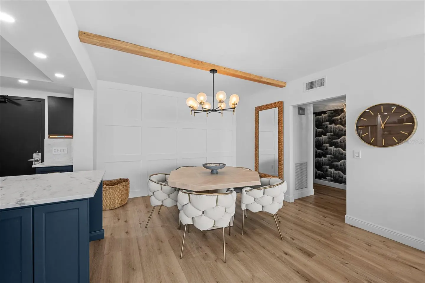 A modern dining area with a light wood table, white chairs, and a black chandelier. A blue kitchen island is visible.