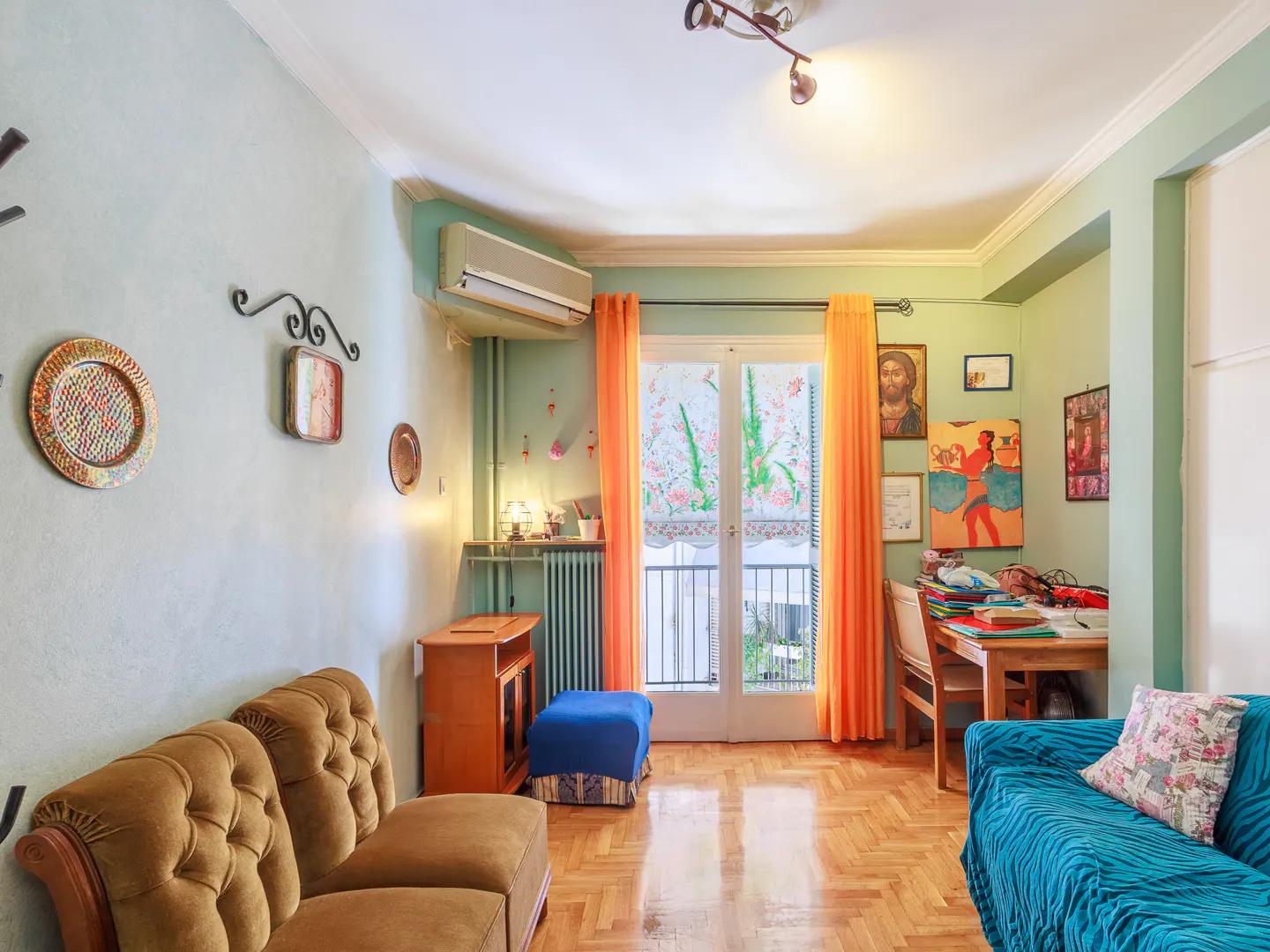 Living room with light green walls, a brown tufted sofa, a blue sofa, orange curtains, and a desk by a balcony door.