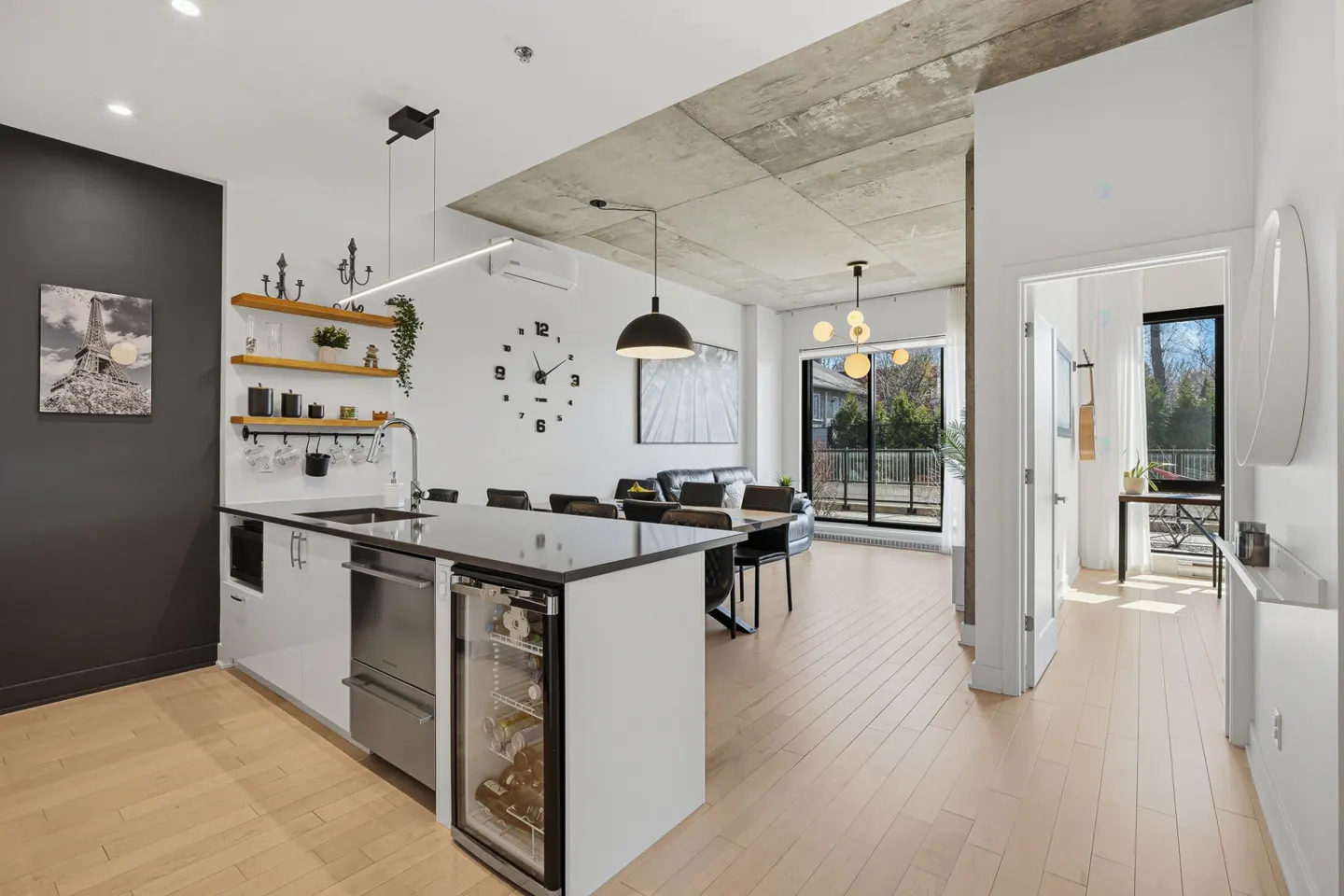 Bright, modern apartment interior with a kitchen island, dining area, and living room. Concrete ceiling and light wood floors.