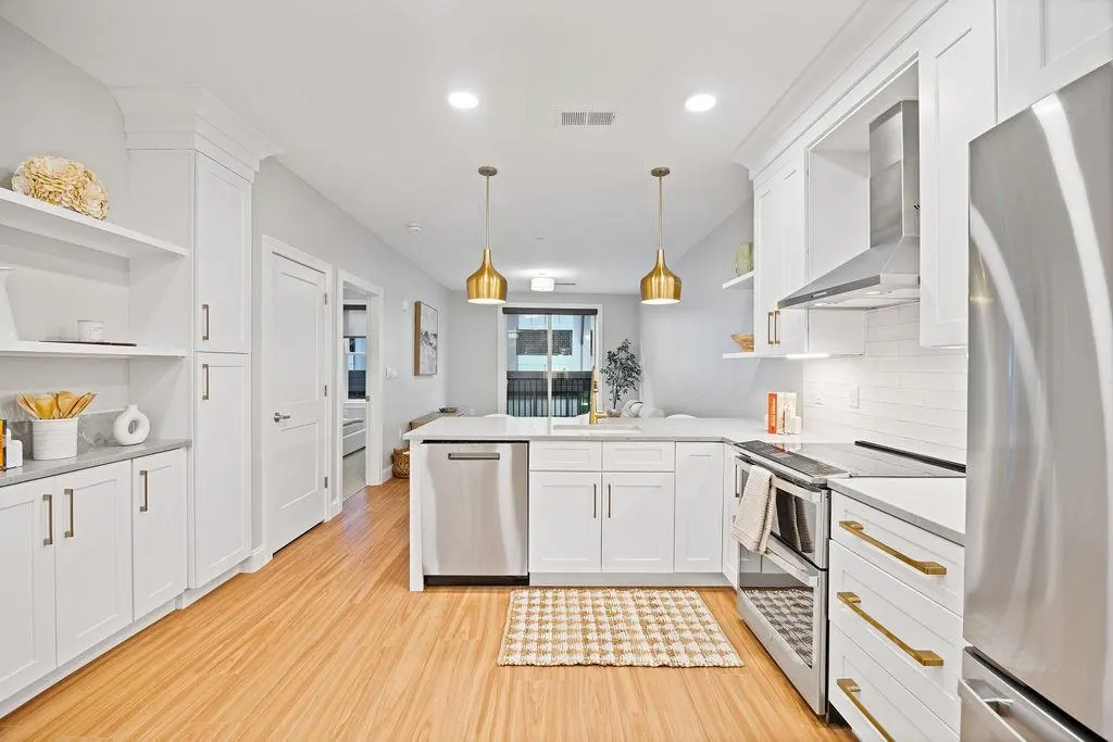 Bright, modern kitchen with white cabinets, stainless steel appliances, and gold pendant lights over an island.