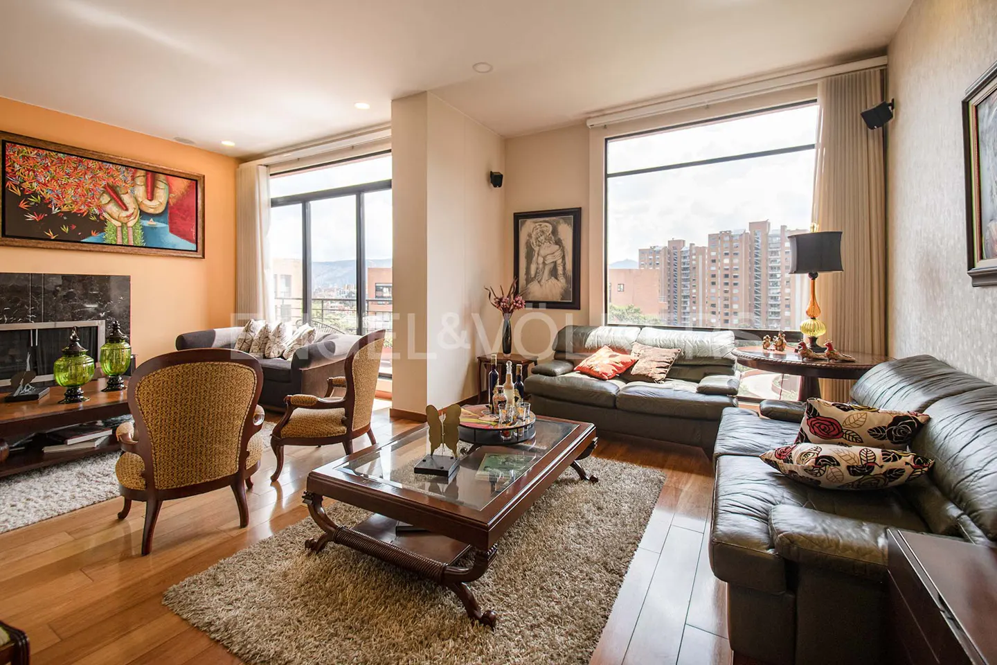 A living room with hardwood floors, a large window, and a brown leather sofa. There is a glass coffee table in the center of the room.