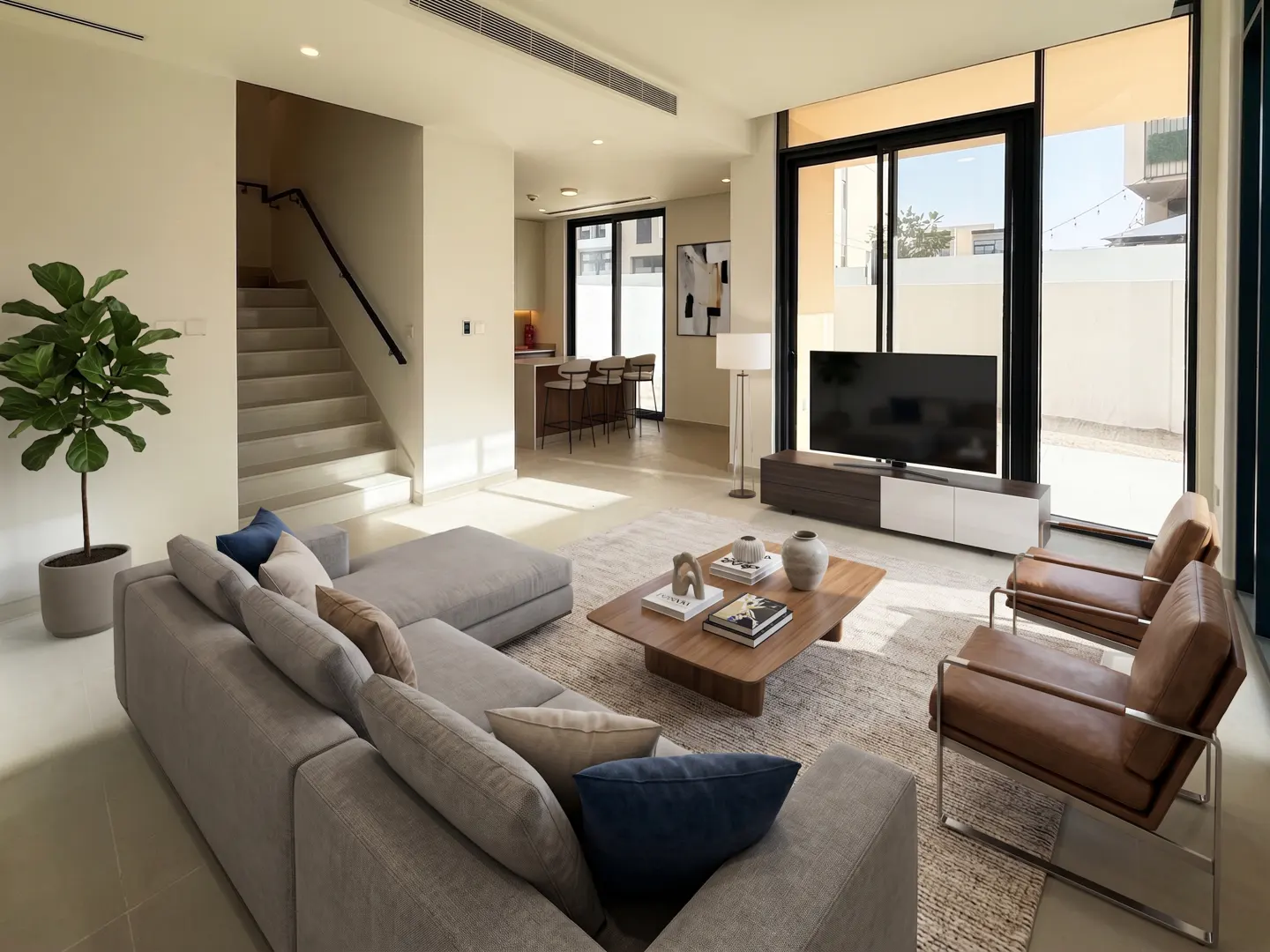 A bright living room with a gray sectional sofa, wood coffee table, TV, and two leather chairs. Stairs lead to another floor.
