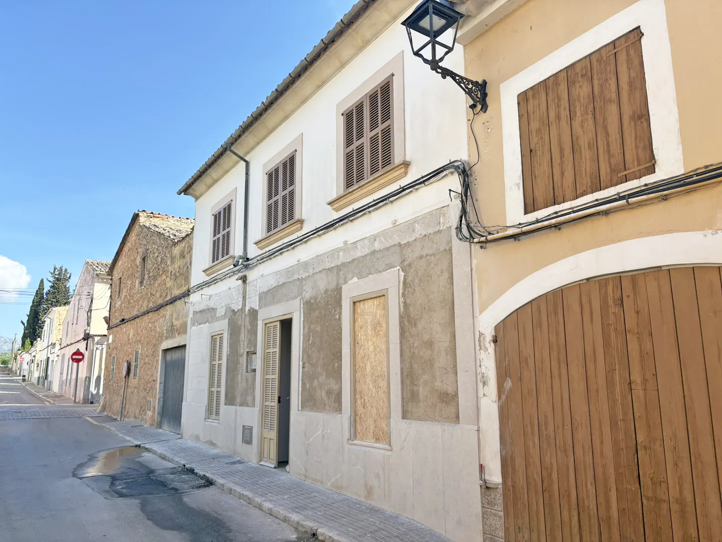 Street view of old, two-story buildings with closed brown shutters and a black street lamp on a sunny day.