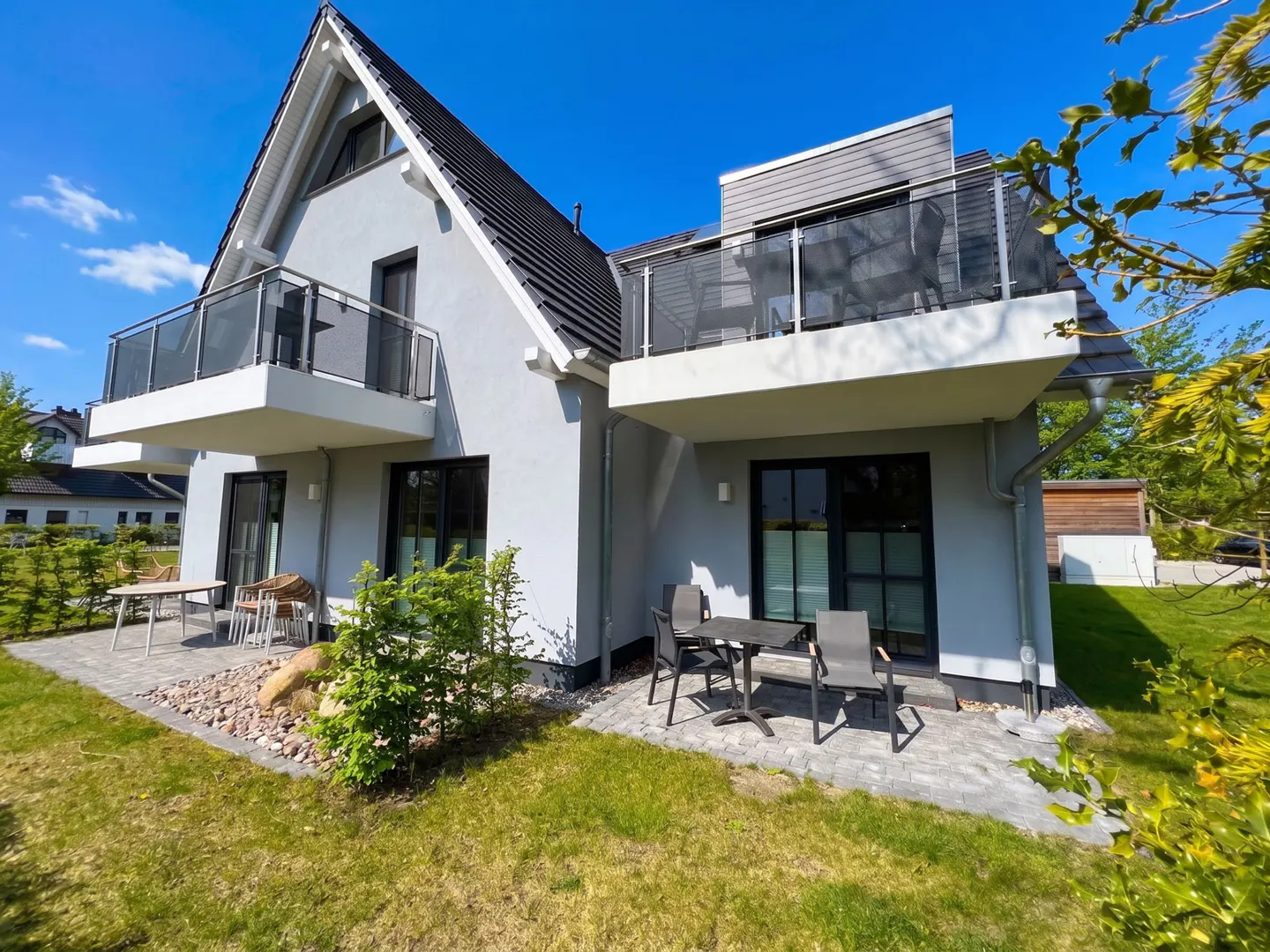 Two-story gray house with black trim, balconies, and outdoor seating on a sunny day.