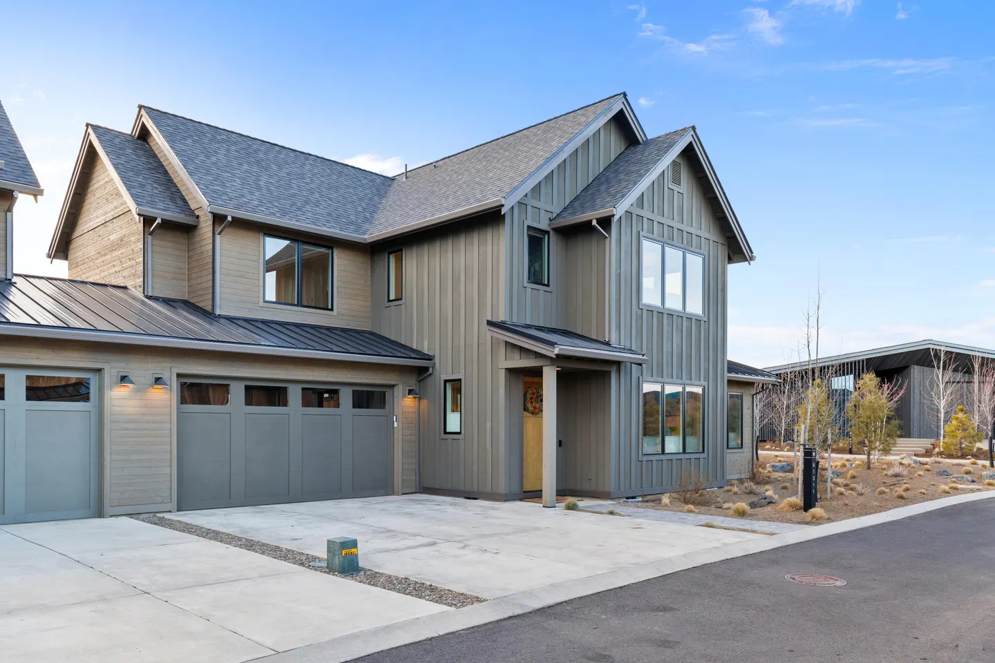 Two-story house with gray siding, a gray roof, and a two-car garage. A concrete driveway leads to the garage and front door. Blue sky.
