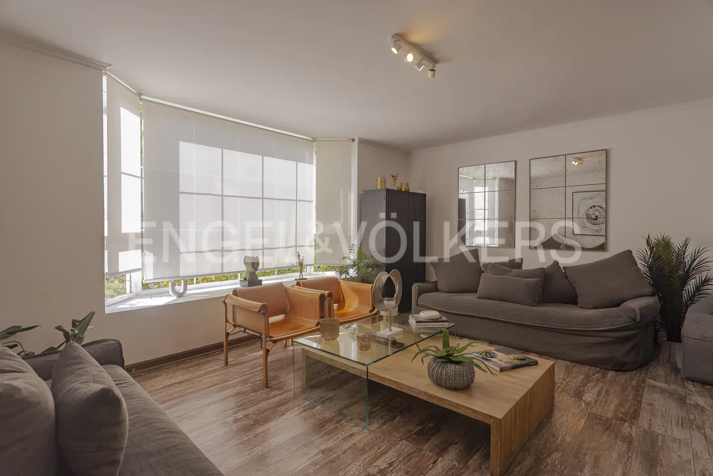 Living room with wood floors, a gray sofa, two tan leather chairs, and a wood and glass coffee table.