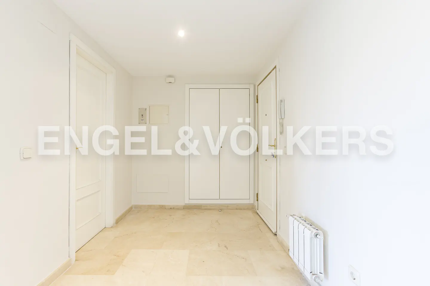 Bright hallway with beige marble floor, white walls, and white doors. A radiator is visible on the right.