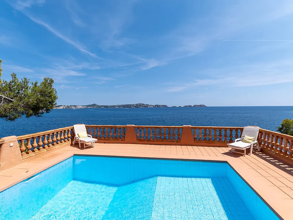 A blue tiled pool overlooks the ocean from a terracotta patio with two white lounge chairs.