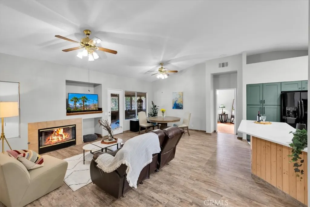 Open-concept living room with a fireplace, TV, brown leather recliner, and a kitchen with green cabinets.