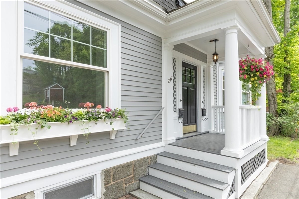 Exterior of a gray house with white trim, a black front door, and a flower box under a large window.