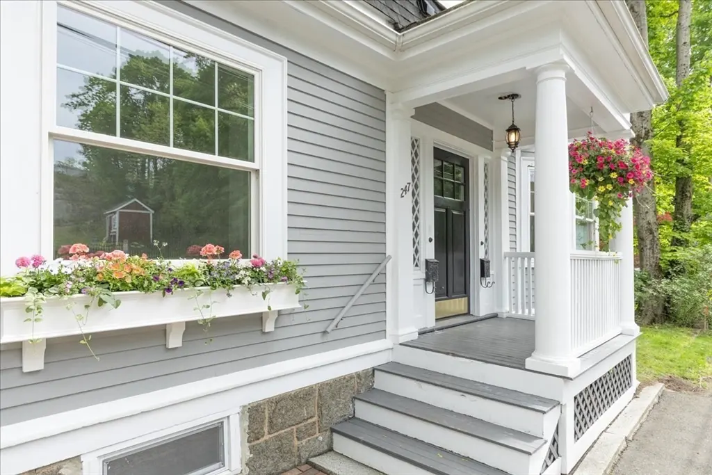Exterior of a gray house with white trim, a black front door, and a flower box under a large window.