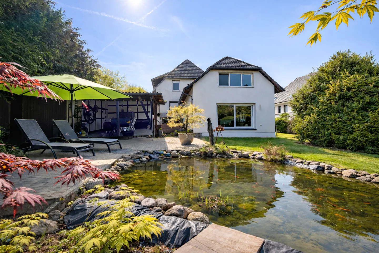 Backyard view of a white house with a pond, lounge chairs, and a green umbrella.