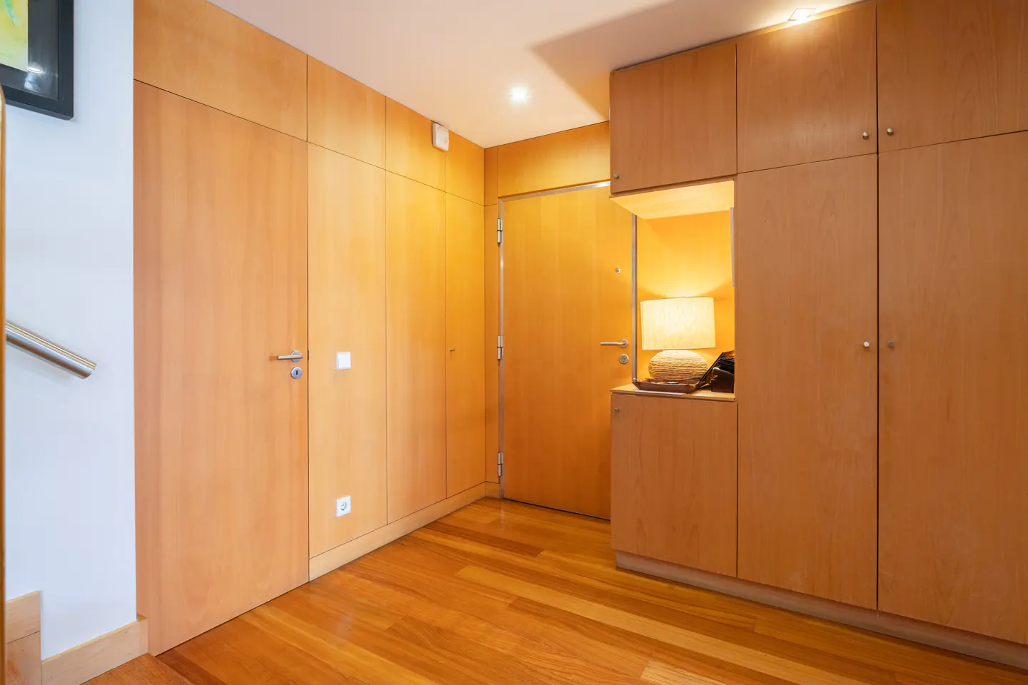 A foyer with light wood floors, doors, and built-in cabinets. A lamp sits on a shelf next to an exterior door.