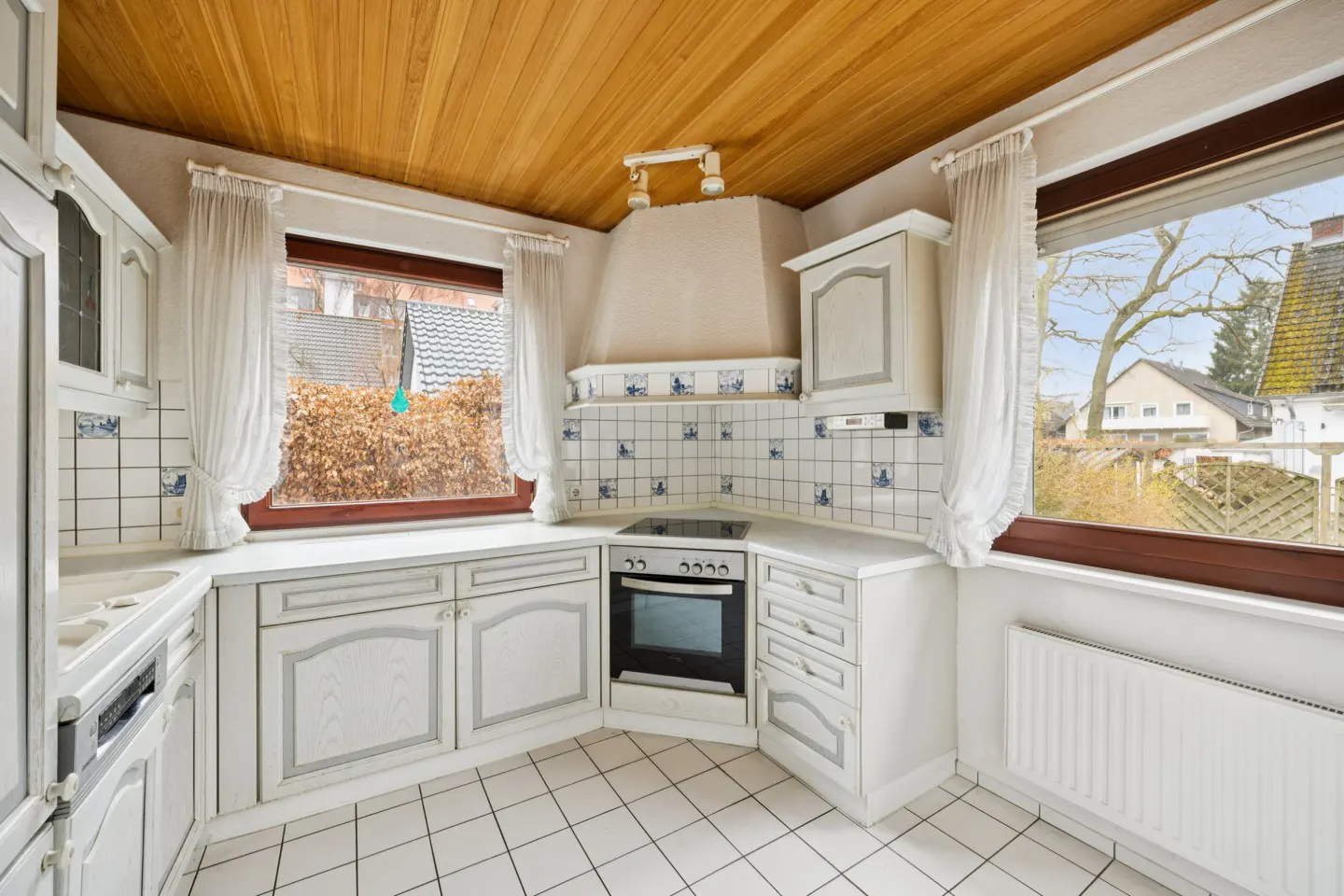 Bright kitchen with white cabinets, tile backsplash, and wood ceiling. Windows with sheer curtains offer outdoor views.
