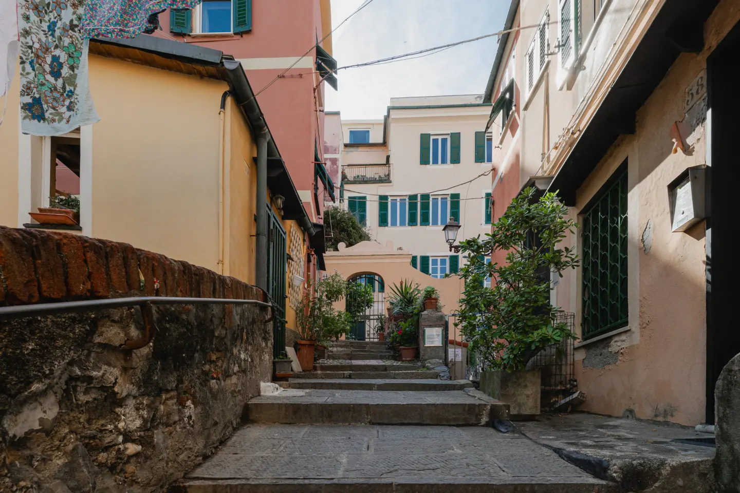 Stone steps lead up a narrow street lined with colorful buildings and potted plants in an Italian town.