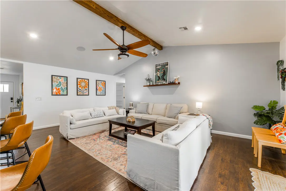 Bright living room with white sofas, dark wood floors, and a ceiling fan. Three floral art prints hang on the wall.