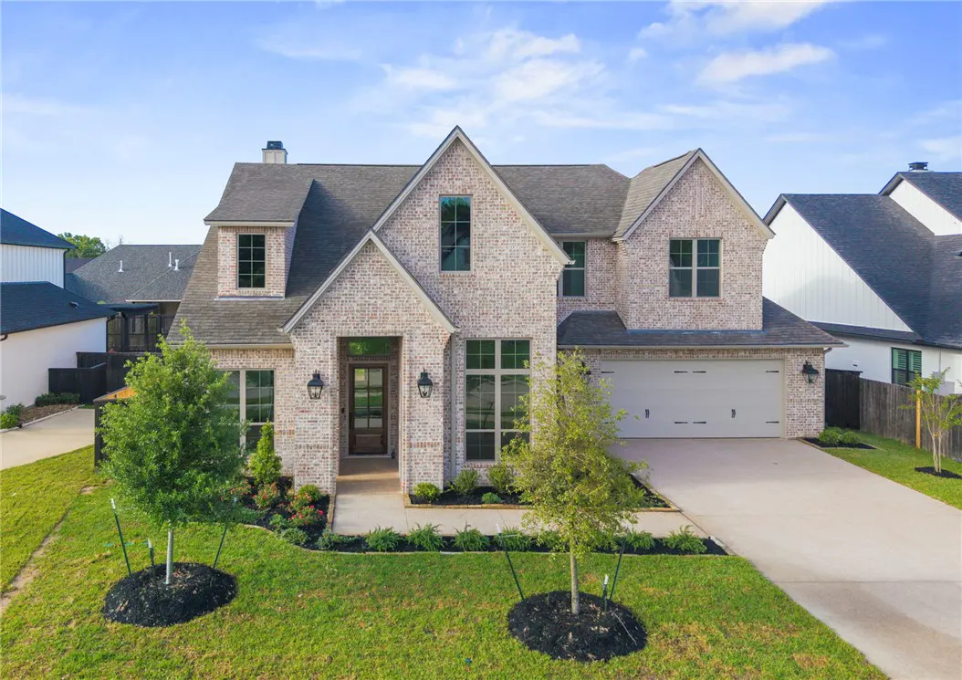 Two-story brick house with a gray roof, a two-car garage, and a green lawn.
