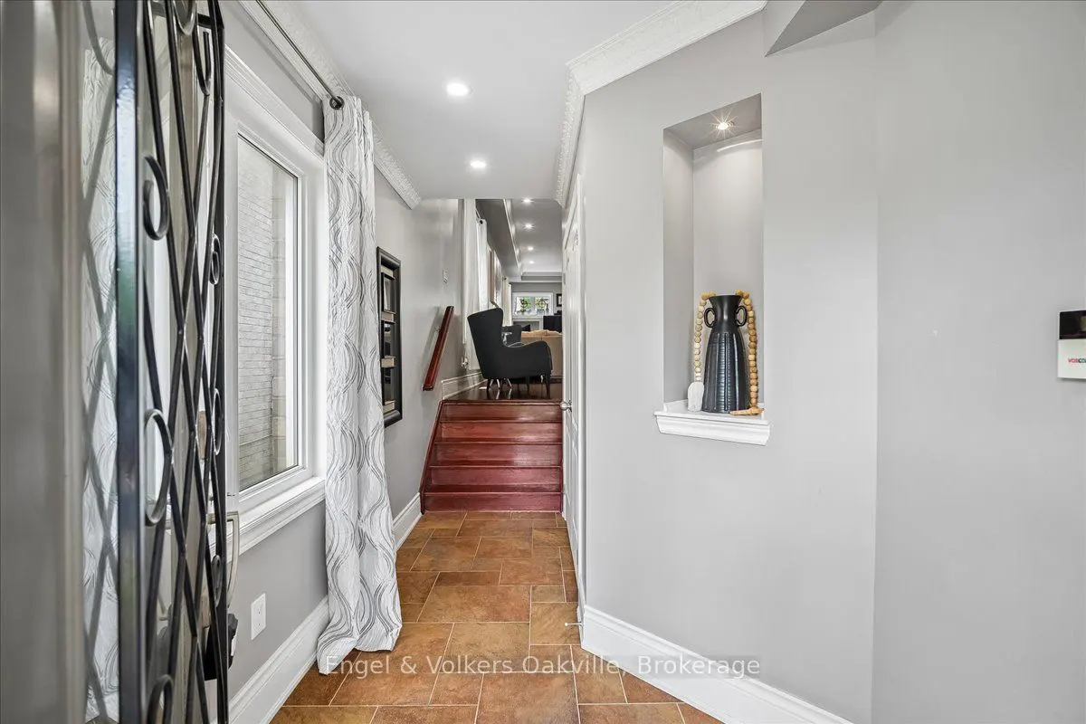 A hallway with tile floors leads to wooden stairs, featuring a wall niche with a vase and a view into a living area.
