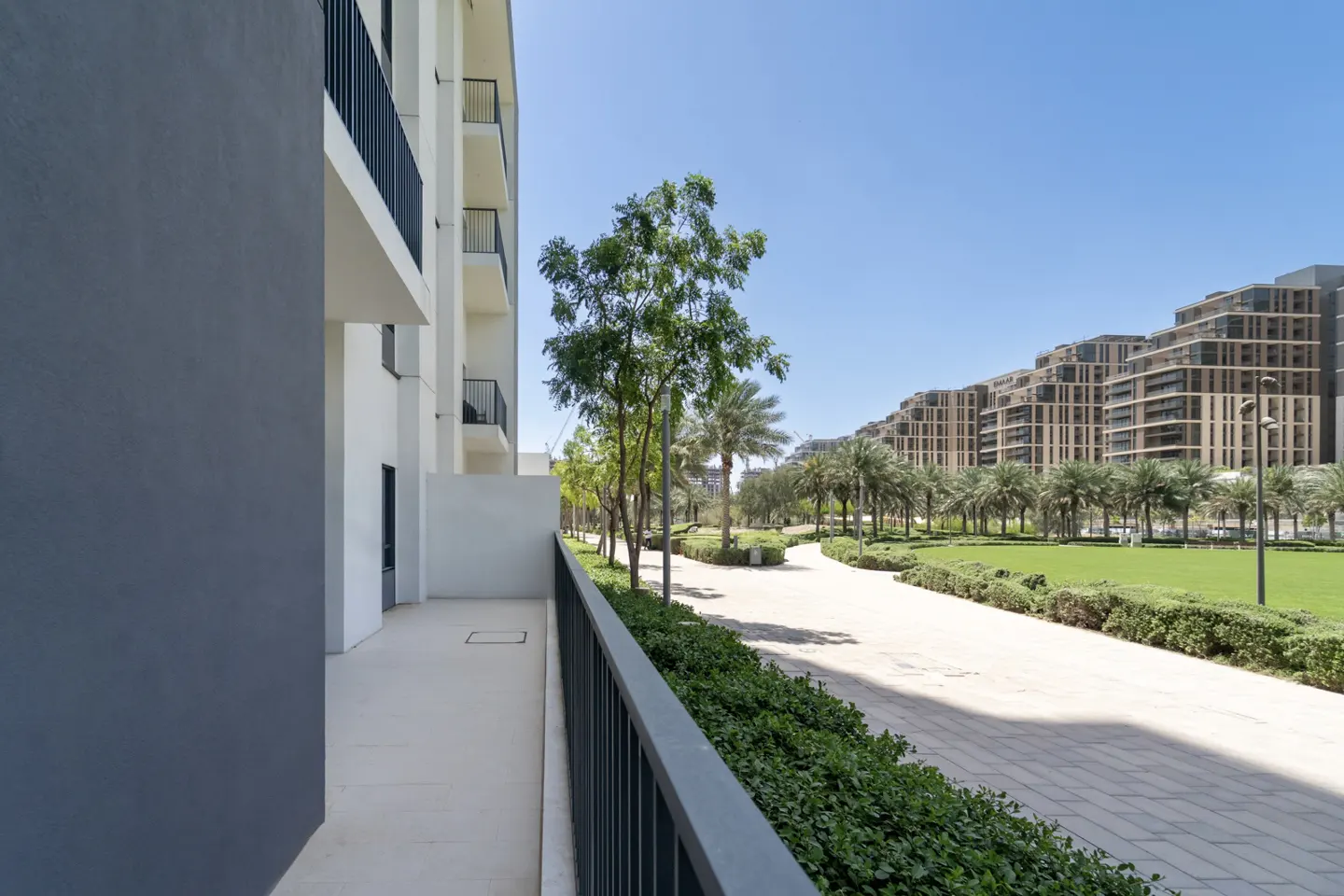 View from a balcony overlooking a landscaped courtyard with palm trees and modern apartment buildings under a clear blue sky.