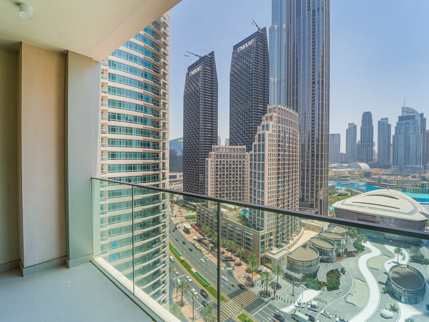 View from a balcony with a glass railing overlooking Dubai skyscrapers and a busy street below.