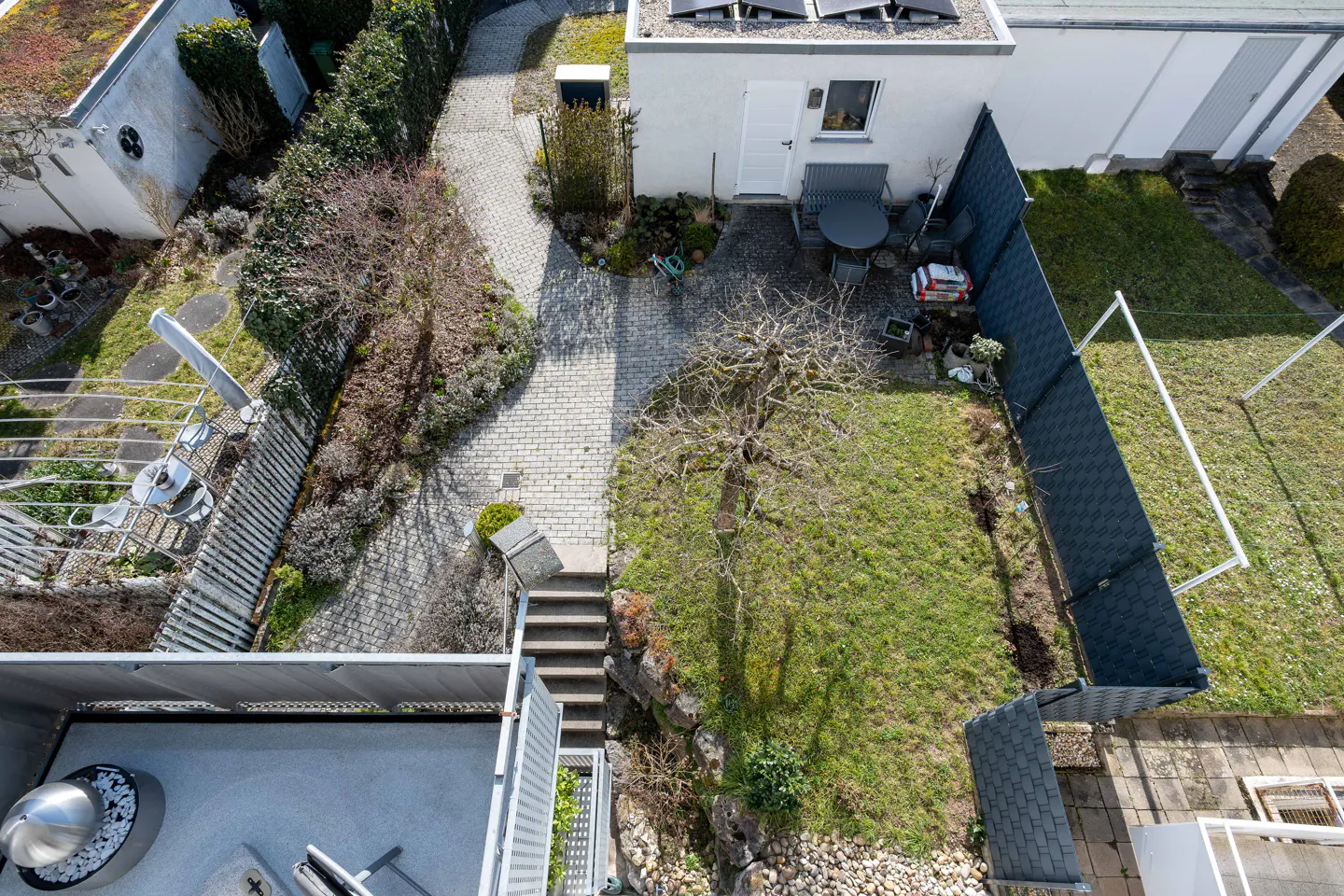 Aerial view of a backyard with a stone path, green grass, and a small white building with solar panels.