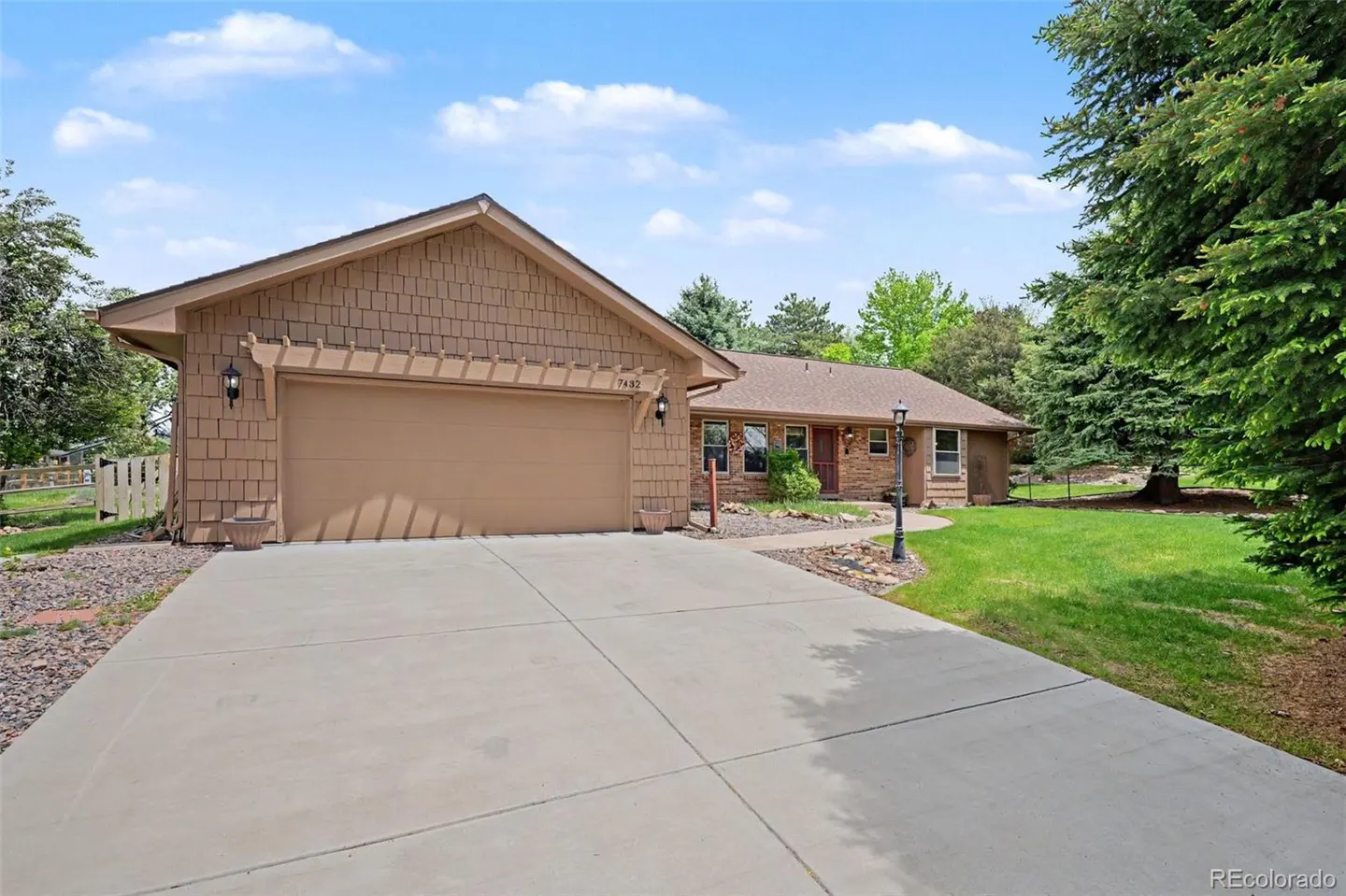 Tan house with a large driveway, attached garage, and green trees in the background.