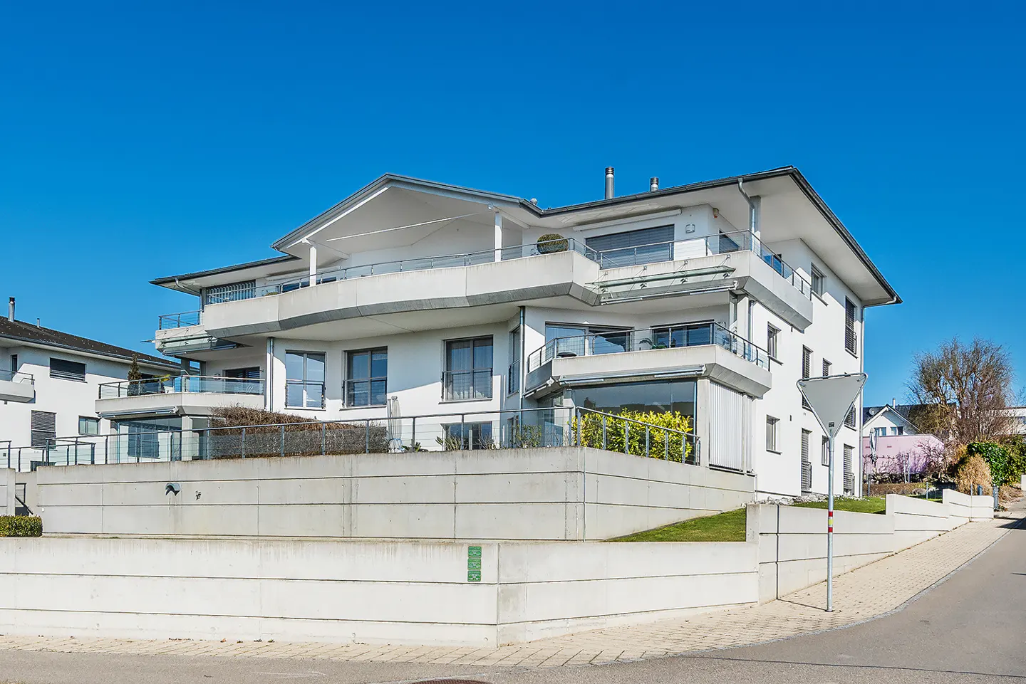Modern white three-story apartment building with balconies under a clear blue sky.