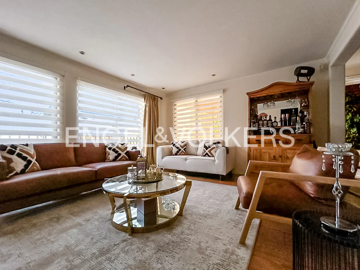 Living room with brown leather sofa, white loveseat, gold coffee table, and wooden bar cabinet.