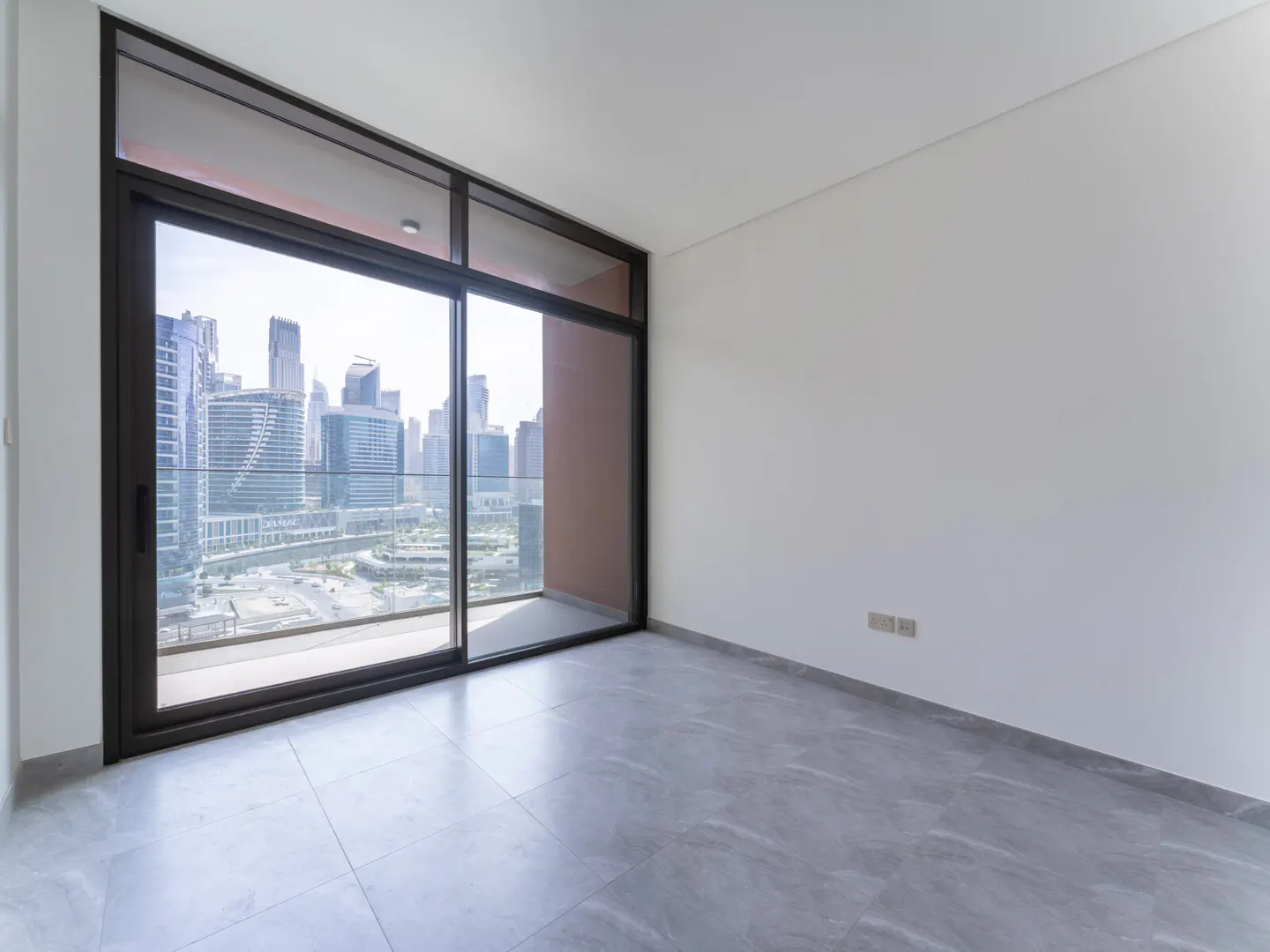 Empty room with gray tile floor, white walls, and a large sliding glass door with a city view.
