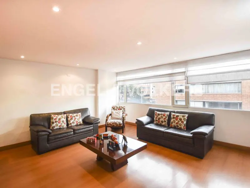 Living room with two brown leather sofas, patterned pillows, a wooden chair, and a dark wood coffee table on a wood floor.